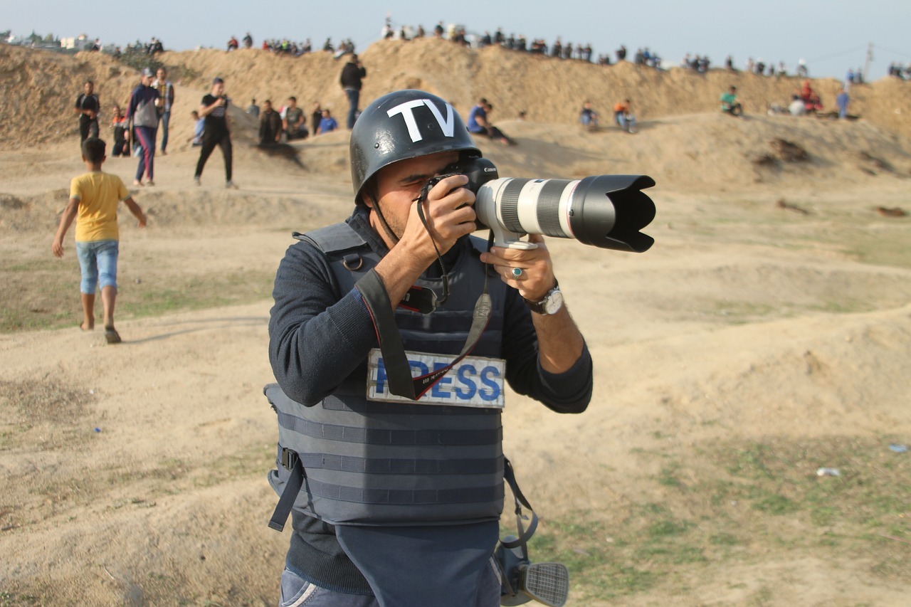  A Reporter in a Press Vest Takes a Photo in a War Zone
