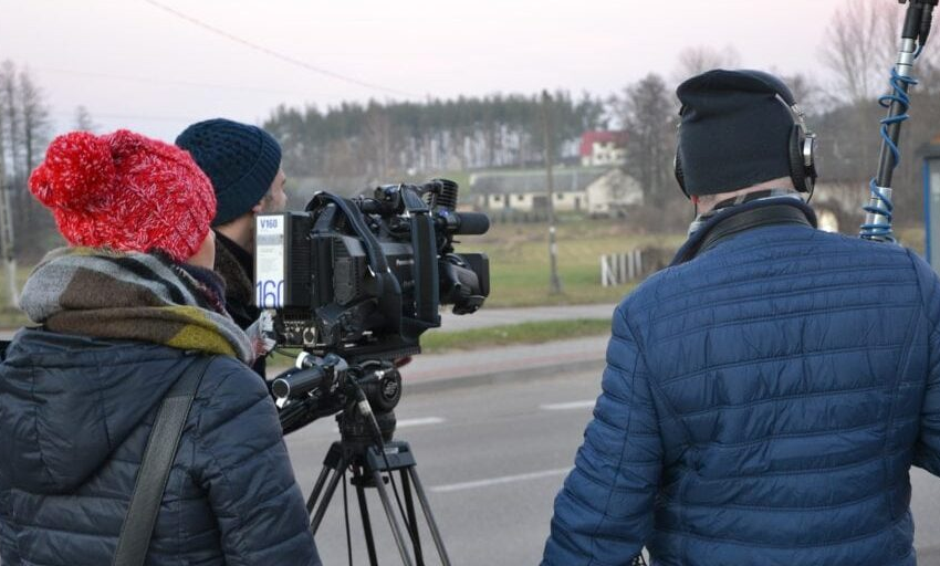 Three people in winter jackets and hates stand outdoors by a camera looking into the distance while recording what we hope is unbiased reporting.