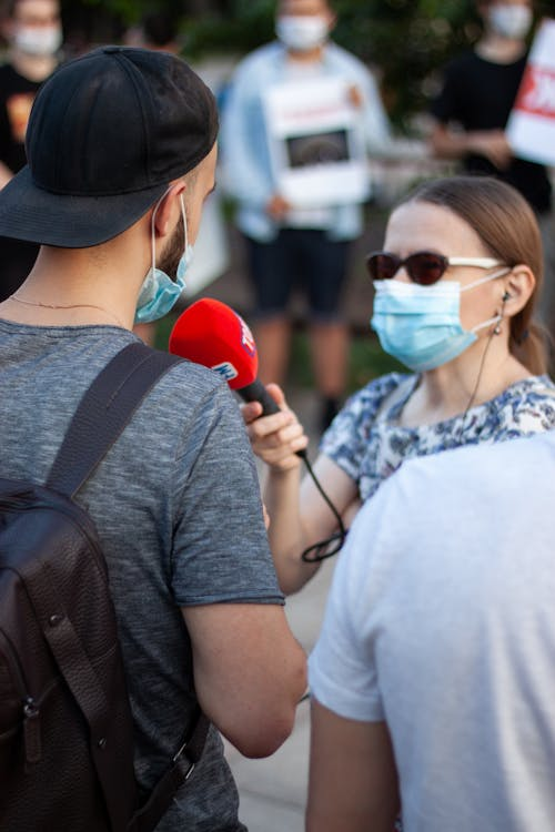 A person with a red microphone interviewing another person on a street 