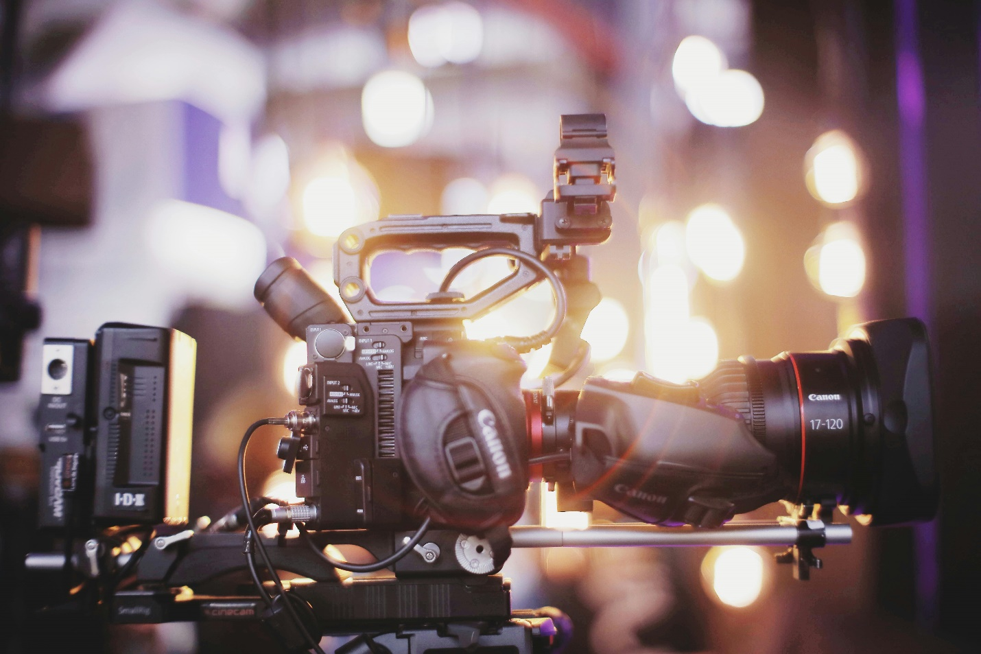 A Canon camera with a large lens and other gadgets pictured in front of lights, creating a buzz similar to that of investigative journalism.