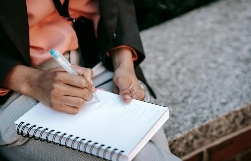 A broadcast journalist taking notes with a pen and notebook by https://www.pexels.com/photo/ethnic-female-employee-writing-list-in-notepad-5999834/