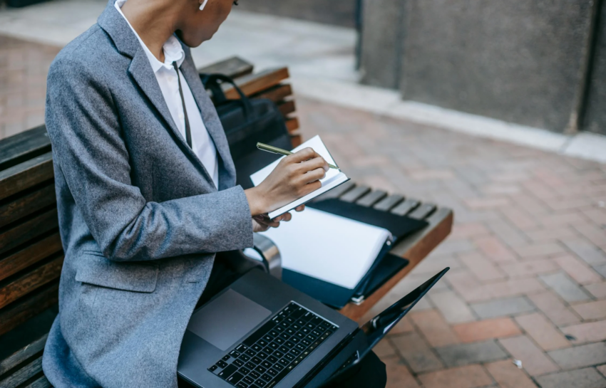 A journalist placement expert taking notes while sitting on a bench by https://www.pexels.com/photo/crop-black-lady-sitting-near-city-buildings-and-working-remotely-6000093/