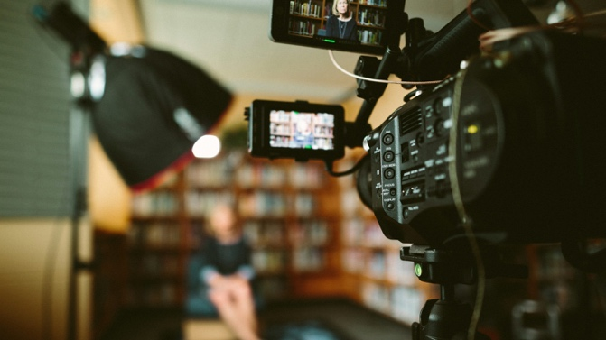 A camera recording a woman sitting in front of a bookshelf